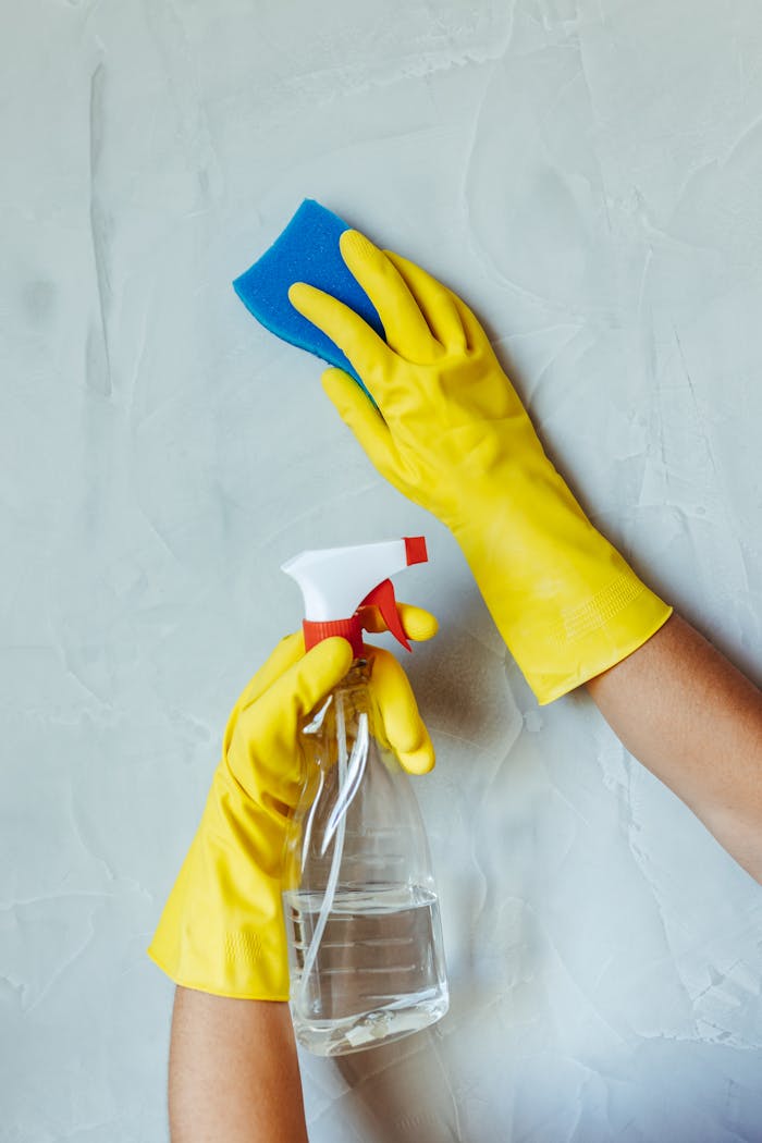 why-choose-us Hands in yellow gloves cleaning wall with sponge and spray bottle.